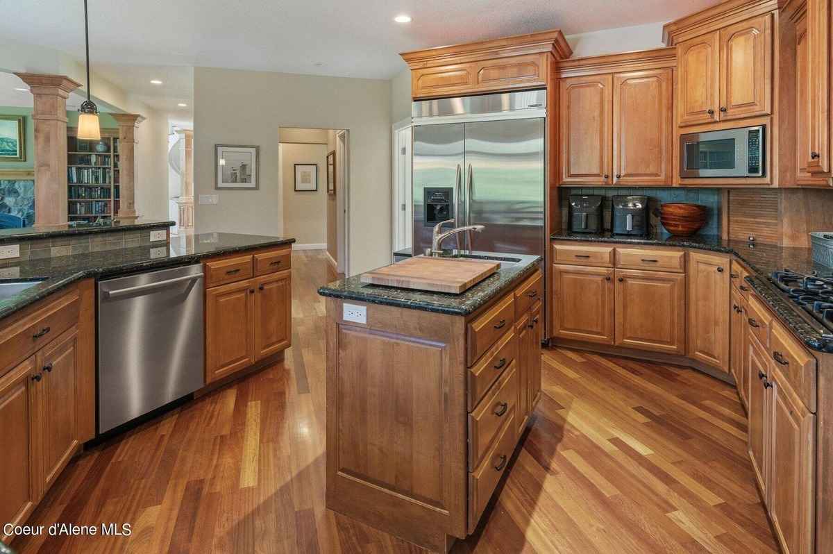 A kitchen with light wood cabinets, dark countertops, and a large island with a cutting board is shown.