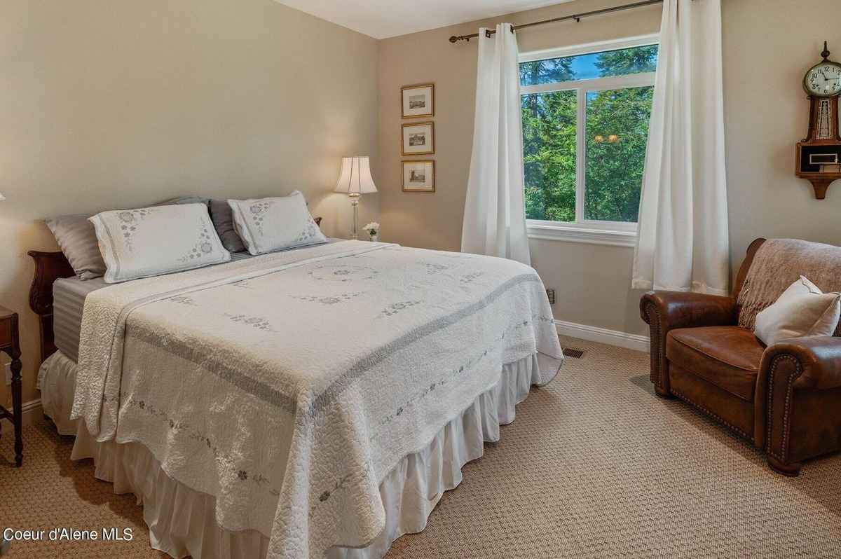 A bedroom with a large bed, a leather chair, and a window with white curtains is shown.