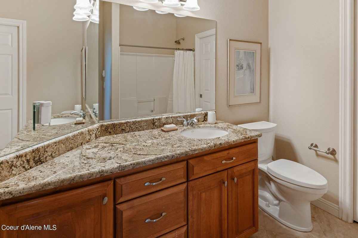 A bathroom with a granite countertop, wood cabinets, and a toilet is shown.