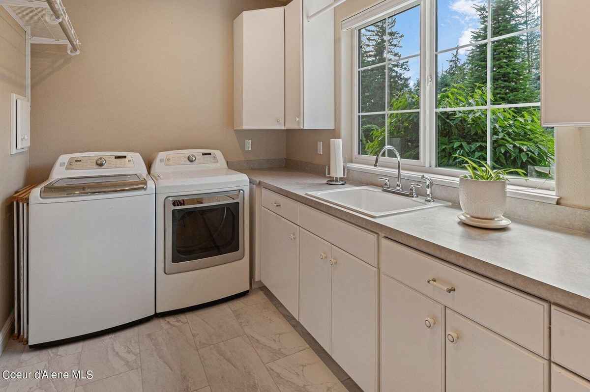 A laundry room with a washer, dryer, sink, and cabinets is shown.