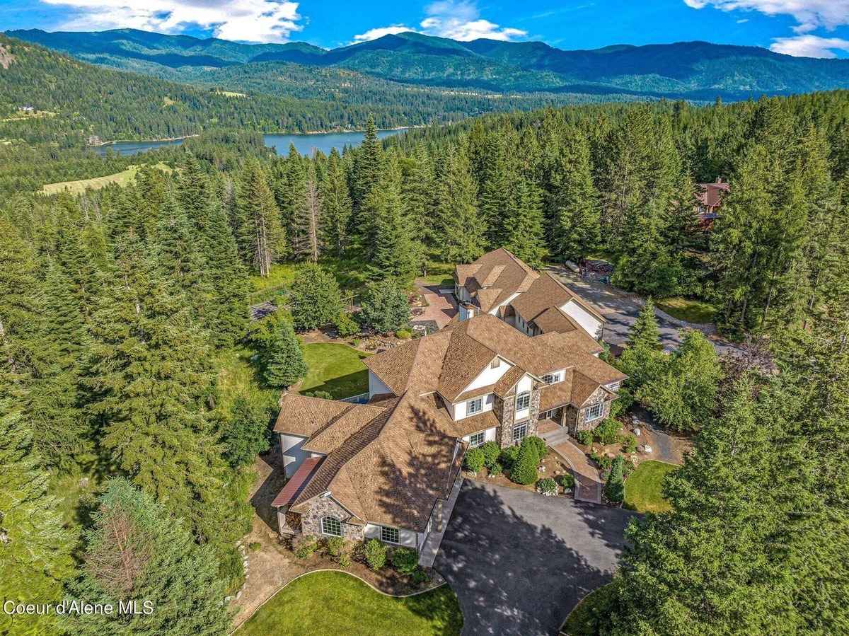 A large house sits in a forest overlooking a lake and mountains. 