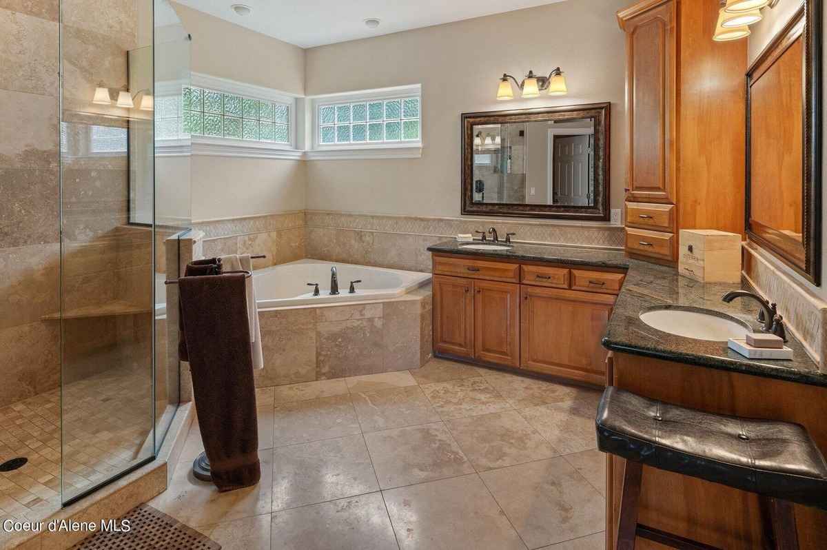 A large bathroom with a corner bathtub, double sinks, and wood cabinets is shown.