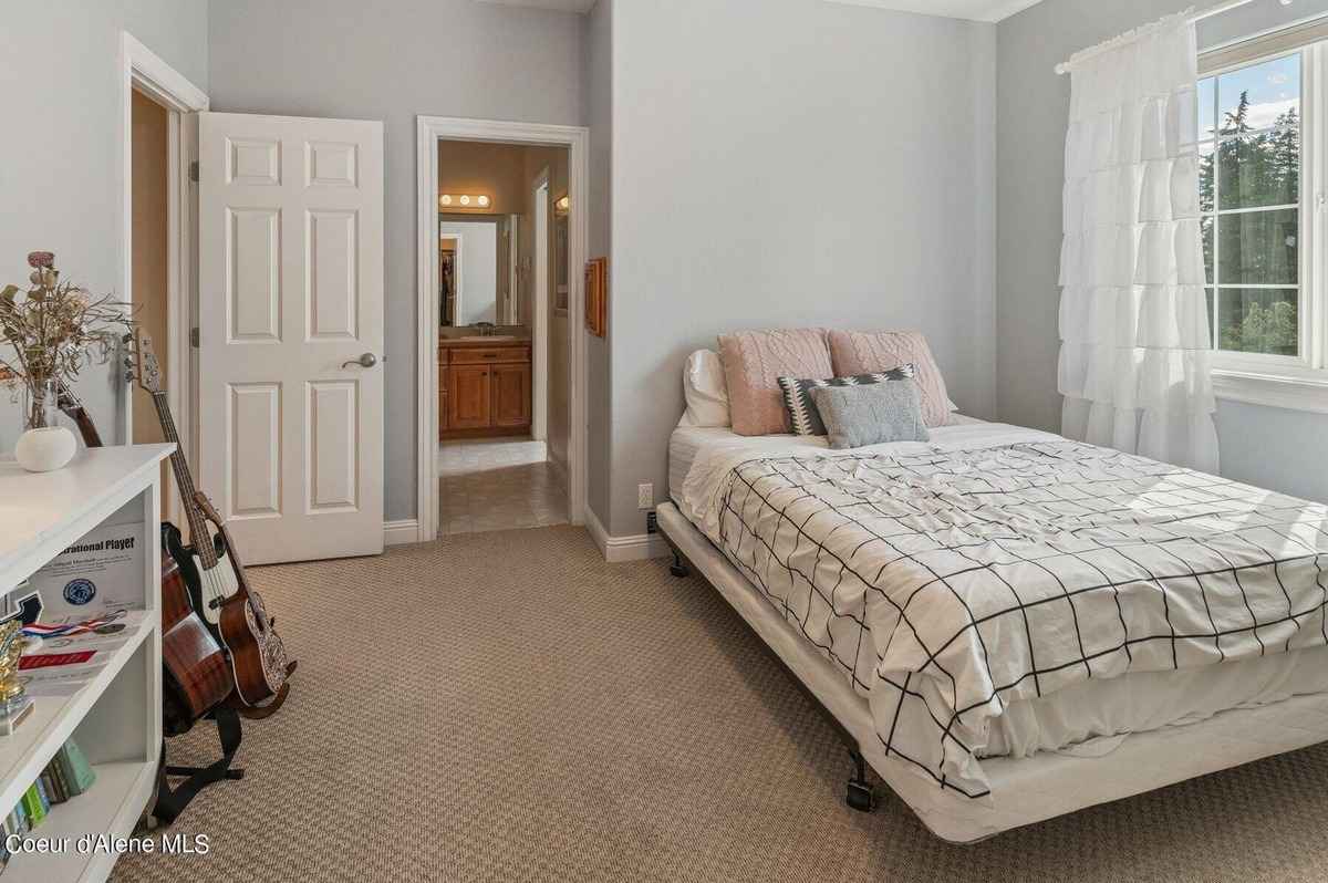 A bedroom with a bed, a bookshelf, and a guitar is shown. A bathroom is visible in the background.