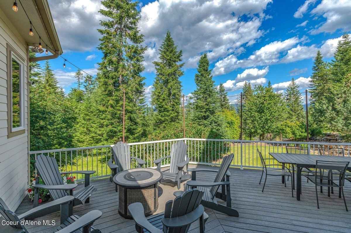 A deck with a fire pit, chairs, and a table is shown, overlooking a wooded area.