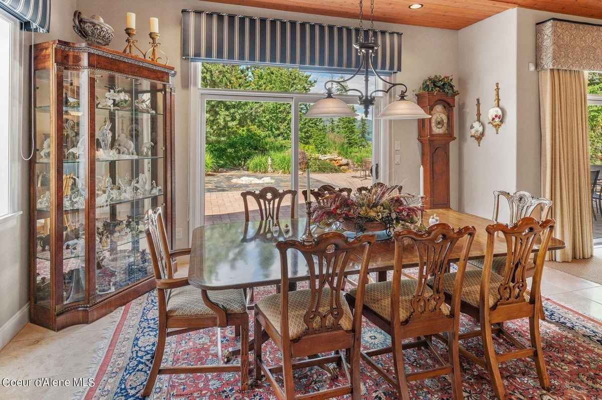 A formal dining room features a large wooden table, chairs, a china cabinet, and sliding glass doors that open to a view of greenery.