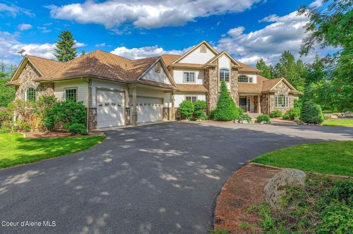 A large, light-colored house with a three-car garage sits on a large paved driveway.