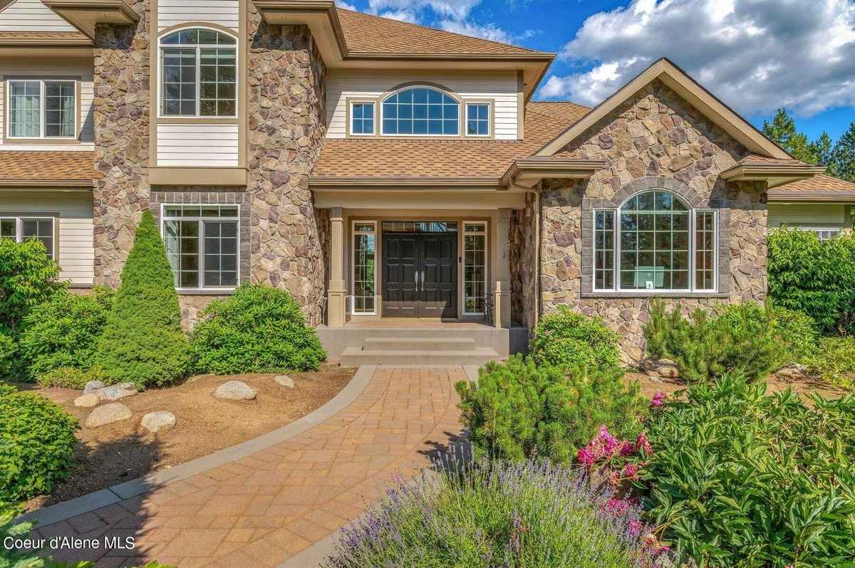 A stone and wood house's entrance features a paved walkway leading to a double dark-colored door.