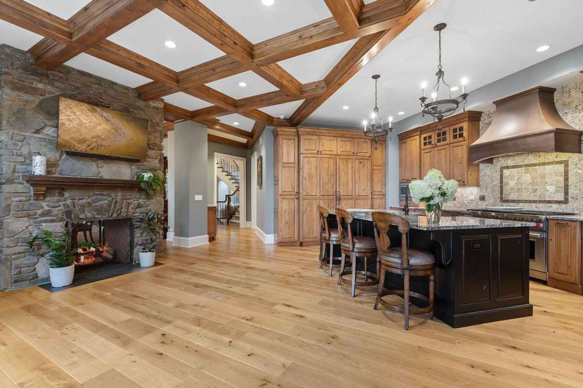  spacious kitchen with wooden cabinetry, a stone fireplace, and coffered wood ceilings.