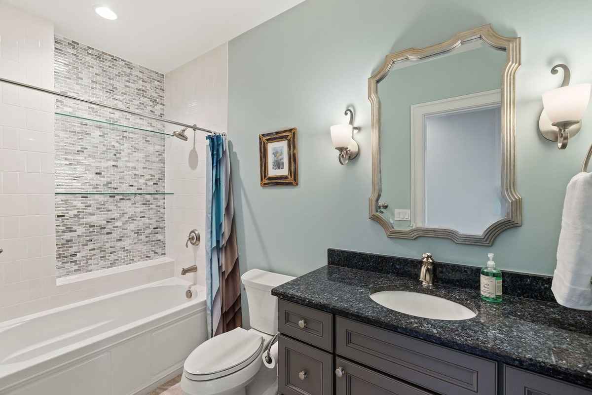 A stylish bathroom featuring a bathtub with a mosaic-tiled backsplash and a granite countertop.