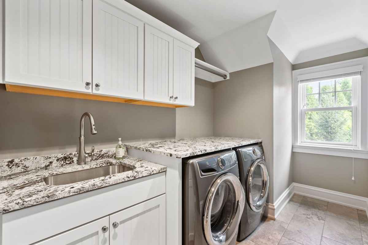 A functional laundry room with granite countertops, a sink, and modern appliances.