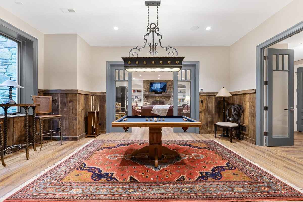 A charming game room with a billiards table, decorative lighting, and rustic wood paneling.