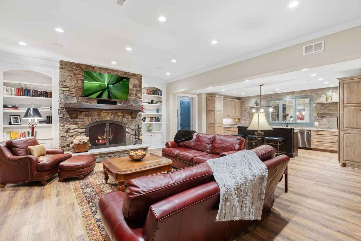 A cozy family room with leather seating, a stone fireplace, and built-in bookshelves.