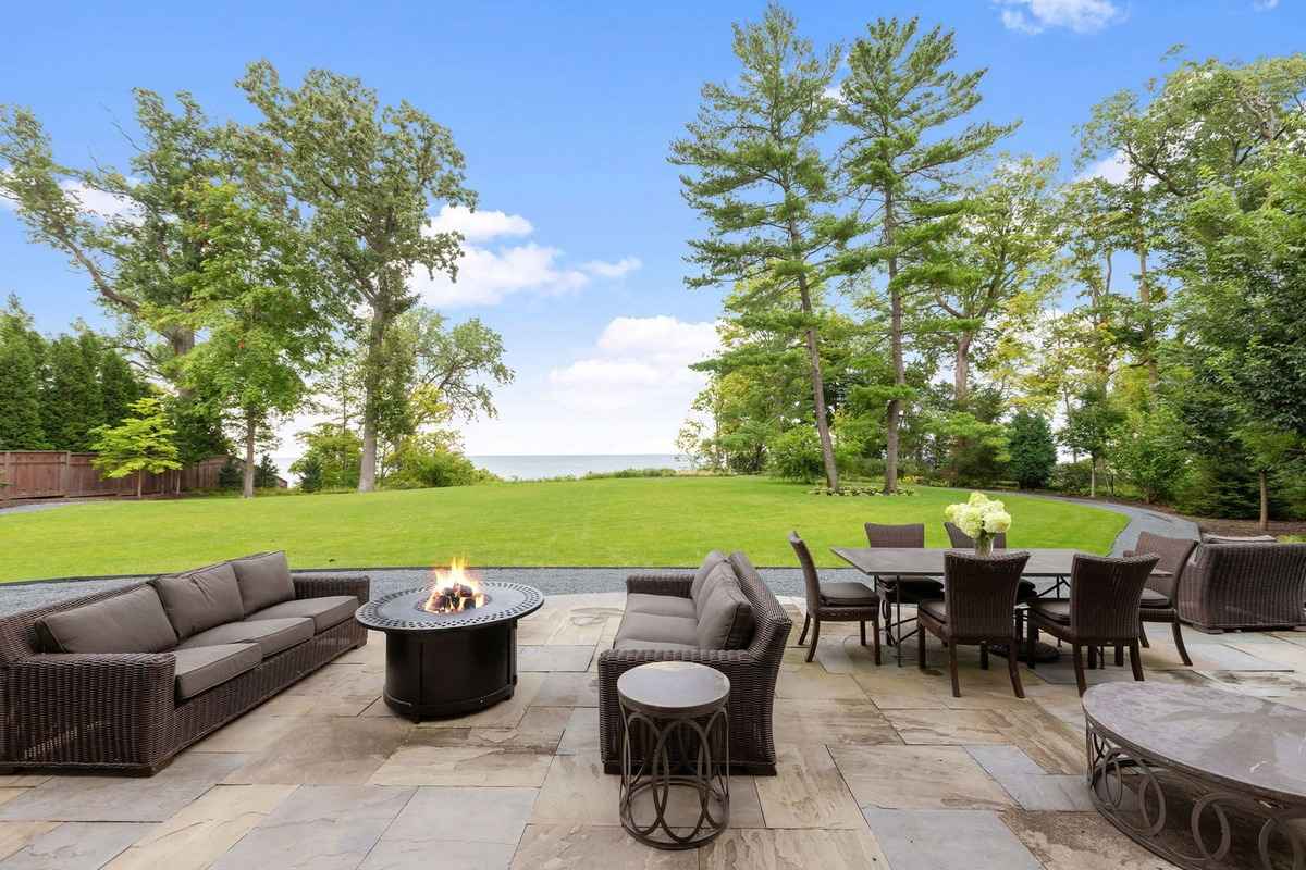 A serene backyard with outdoor seating and a fire pit overlooking a large lawn and trees.