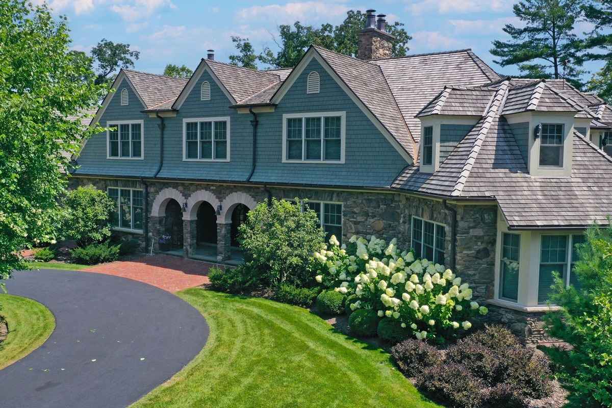 A charming stone and shingle-style home with arched entryways, manicured landscaping, and a circular driveway.