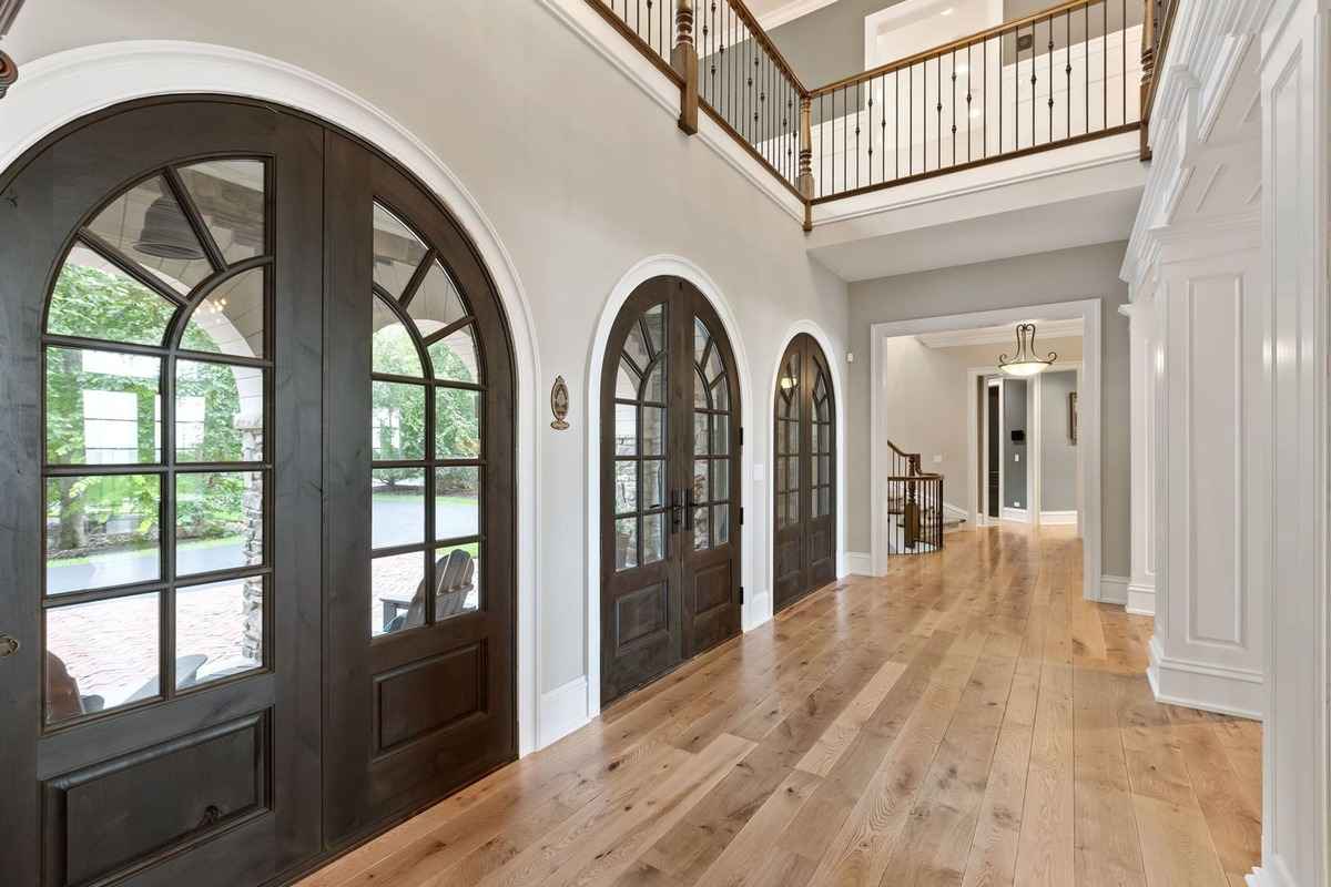 A grand hallway with arched wooden doors and an elegant staircase leading to an upper level.