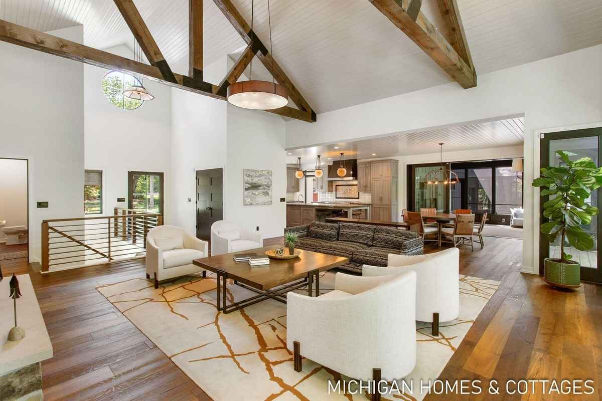 A large, open-concept living area with exposed wooden beams, hardwood floors, and modern furniture is shown.