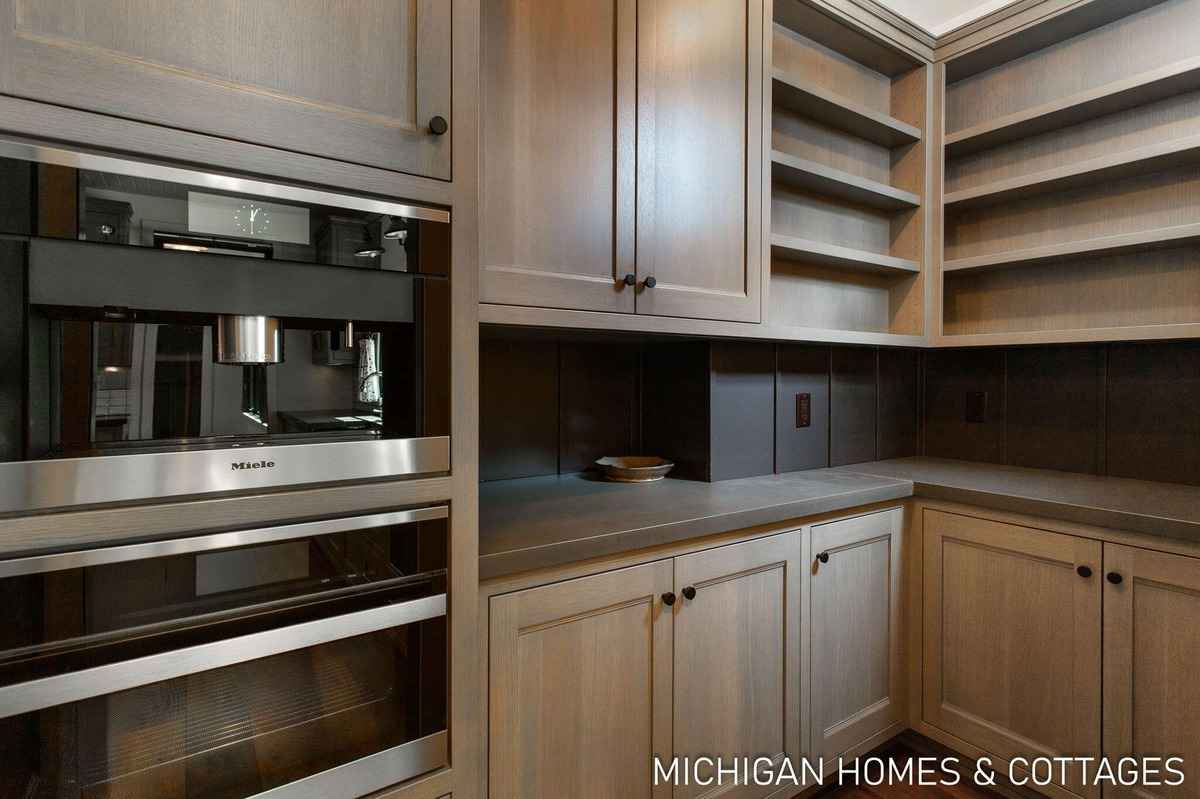 A kitchen features light-colored cabinets, open shelving, and built-in appliances, including a coffee maker and oven.