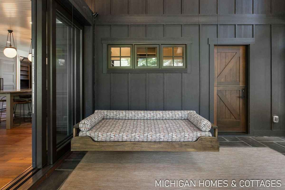 A dark-walled room features a built-in dog bed, sliding glass doors, and a rustic wooden door.