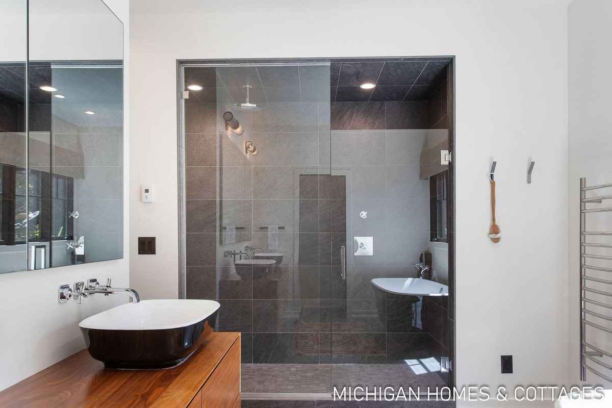 A modern bathroom features a dark-colored vessel sink, a glass-enclosed shower, and a freestanding bathtub.