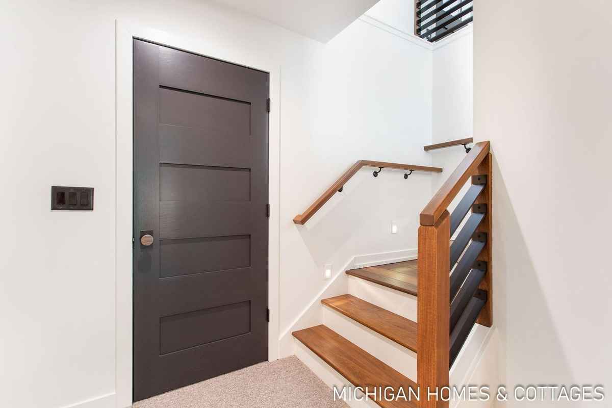 A dark-colored interior door is shown next to a staircase with a modern wooden and metal railing.