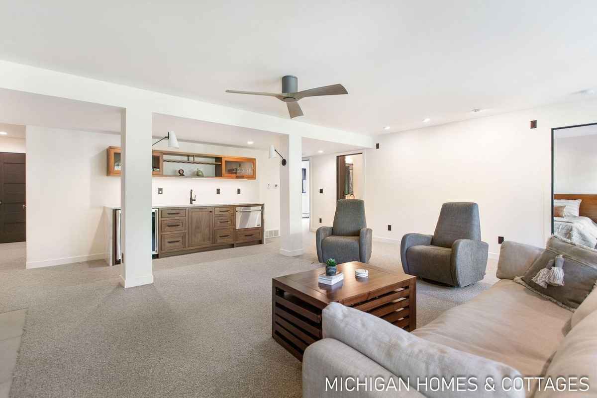 A spacious basement room with a kitchenette, seating area, and a ceiling fan is shown.