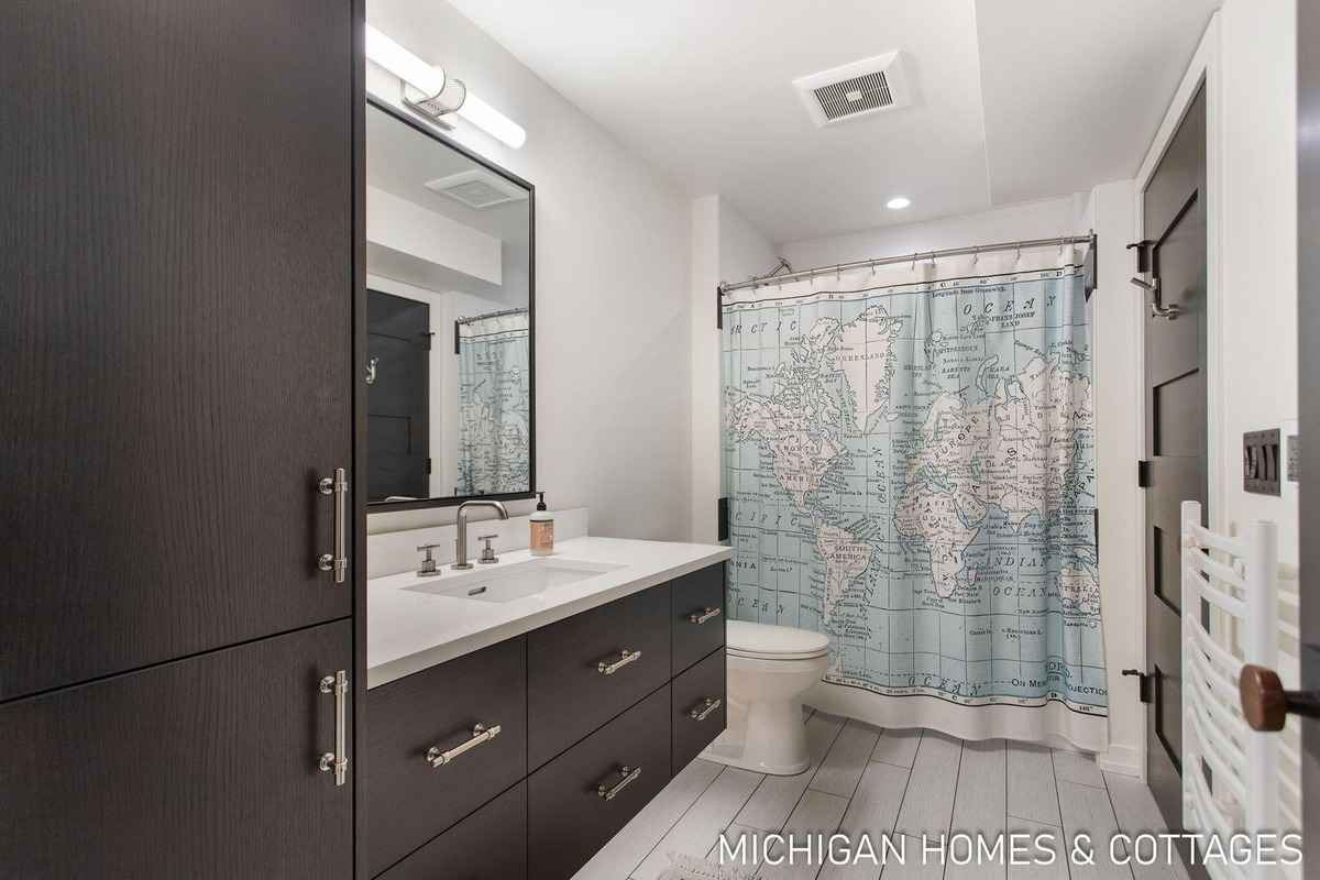 A bathroom with dark brown cabinets, a white countertop, and a world map shower curtain is shown.