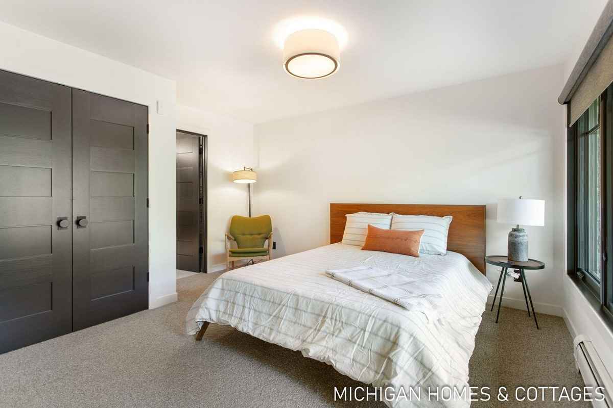 A bedroom with a bed, a small side table, and dark-colored double doors is shown.