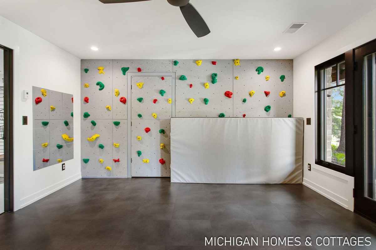 A room with a climbing wall, a padded barrier, and a dark floor is shown.