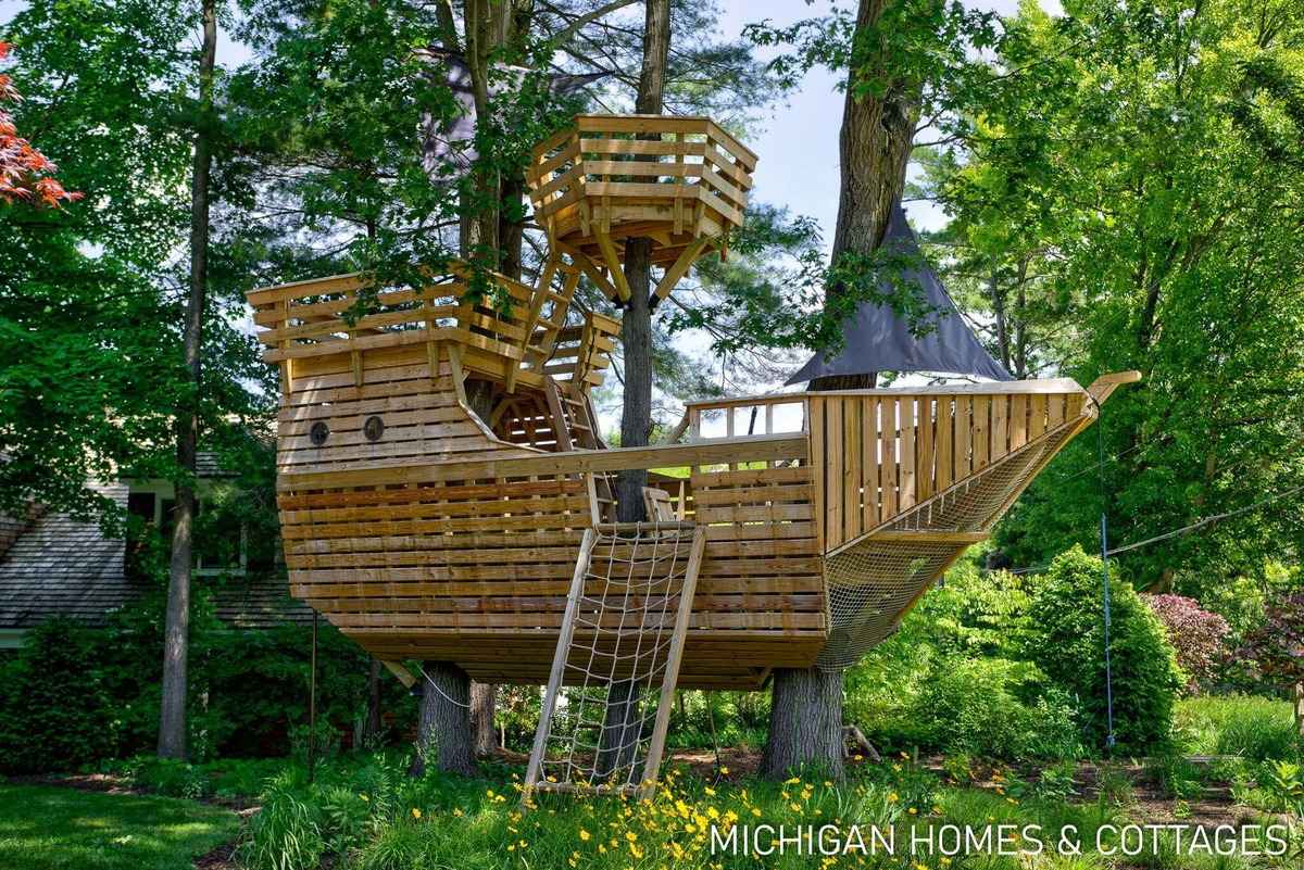 A large, elaborate wooden treehouse built to resemble a ship is shown.