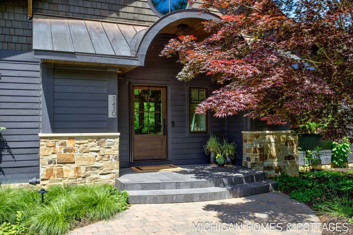 A dark gray house's entrance features a stone-accented porch, a wooden door, and a Japanese maple tree.