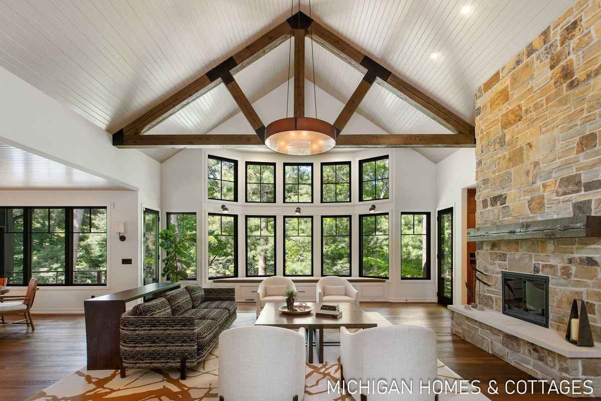 A spacious living room boasts a large window wall, exposed wooden beams, and a stone fireplace.