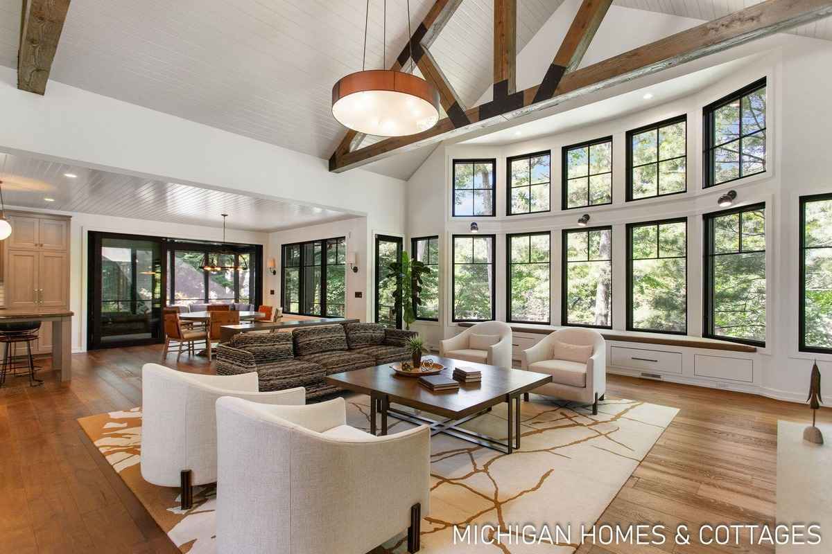 A large, open-plan living area features a wall of windows, exposed wooden beams, and contemporary furniture.