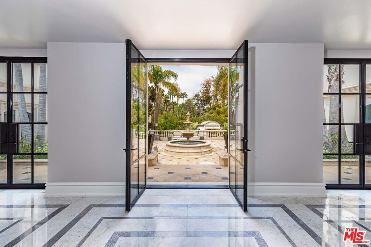 A pair of large, open French doors leading to a courtyard with a fountain. The interior features a light-colored floor with a geometric pattern.