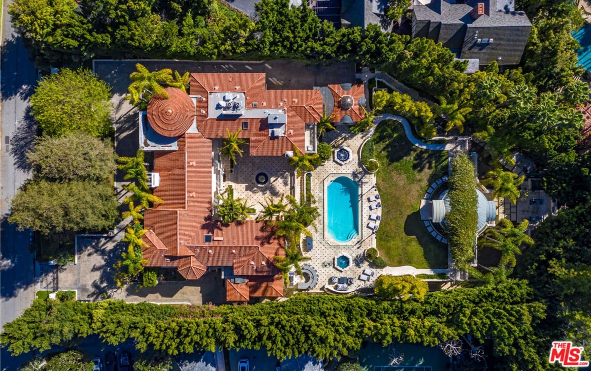 Mansion house has a distinctive reddish-brown roof and a central, domed structure. There's a swimming pool and surrounding landscaping visible.