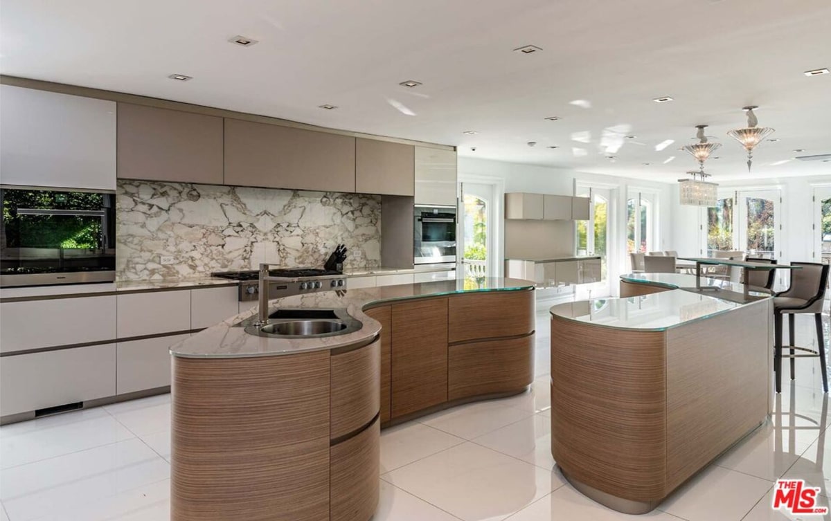 Kitchen with a curved island in the center. The kitchen features light-colored cabinetry, a stone backsplash, and high-end appliances.