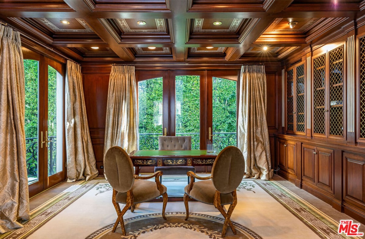 Richly appointed office. Dark wood paneling, a coffered ceiling, and elegant chairs create a formal atmosphere. Large windows allow natural light to enter the room.