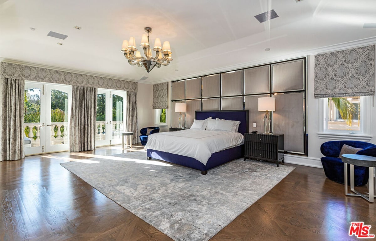 Master bedroom with a navy blue bed, a large area rug, and floor-to-ceiling windows with drapes. The headboard features a unique panel design.