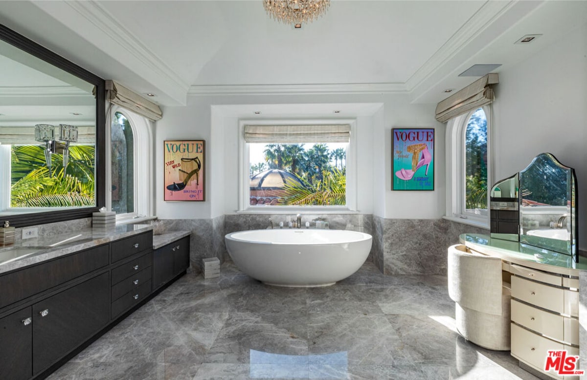 Bathroom with free-standing bathtub, dark gray vanities, and marble flooring. Vogue magazine covers are displayed on the walls.