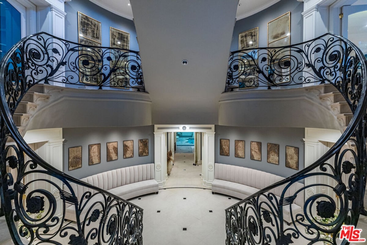 Curved staircase with an ornate, wrought-iron railing. The staircase is in a large, open foyer or entryway with a teal-colored wall.