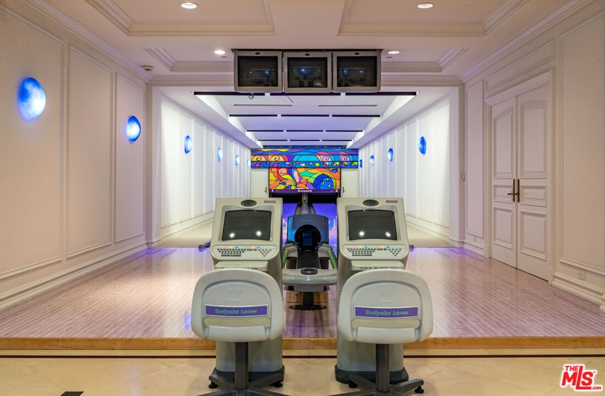 A private indoor bowling alley. The alley is long and narrow with white walls and light-colored flooring. Two automated bowling machines are positioned at the end of the alley.