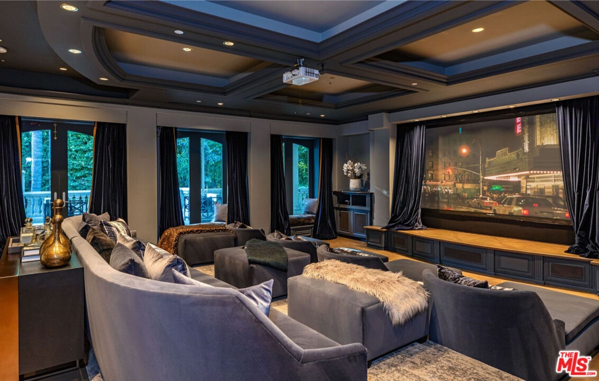 Home theatre or media room. It features a large screen, comfortable seating arranged in a semi-circular fashion, and floor-to-ceiling windows with dark curtains.