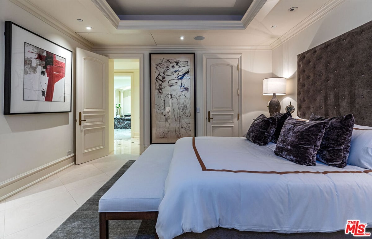 Master bedroom has light-colored linens and dark velvet pillows. There are two large pieces of artwork on the walls.