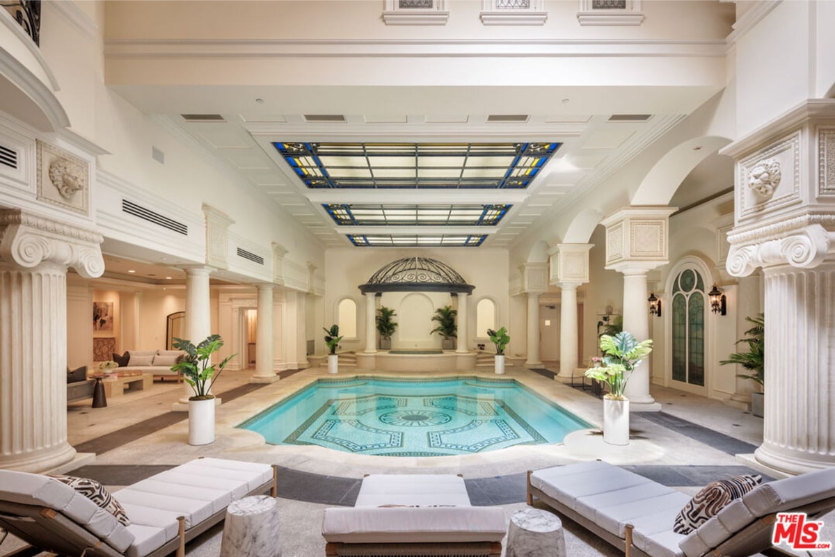 Indoor swimming pool in a large, luxurious home or spa. The pool is surrounded by white columns and has a classical or Roman-inspired design.