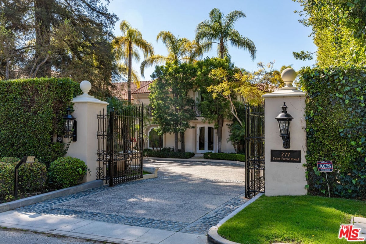 Gate entrance upscale home. The gates are black metal, and the entryway is lined with manicured hedges and landscaping.