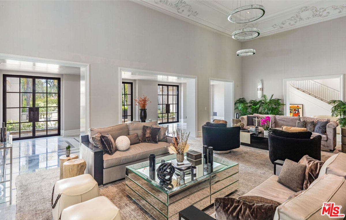 Living room with high ceilings and multiple seating areas. The room is decorated in a neutral color scheme with light-colored sofas and armchairs arranged around a large coffee table.