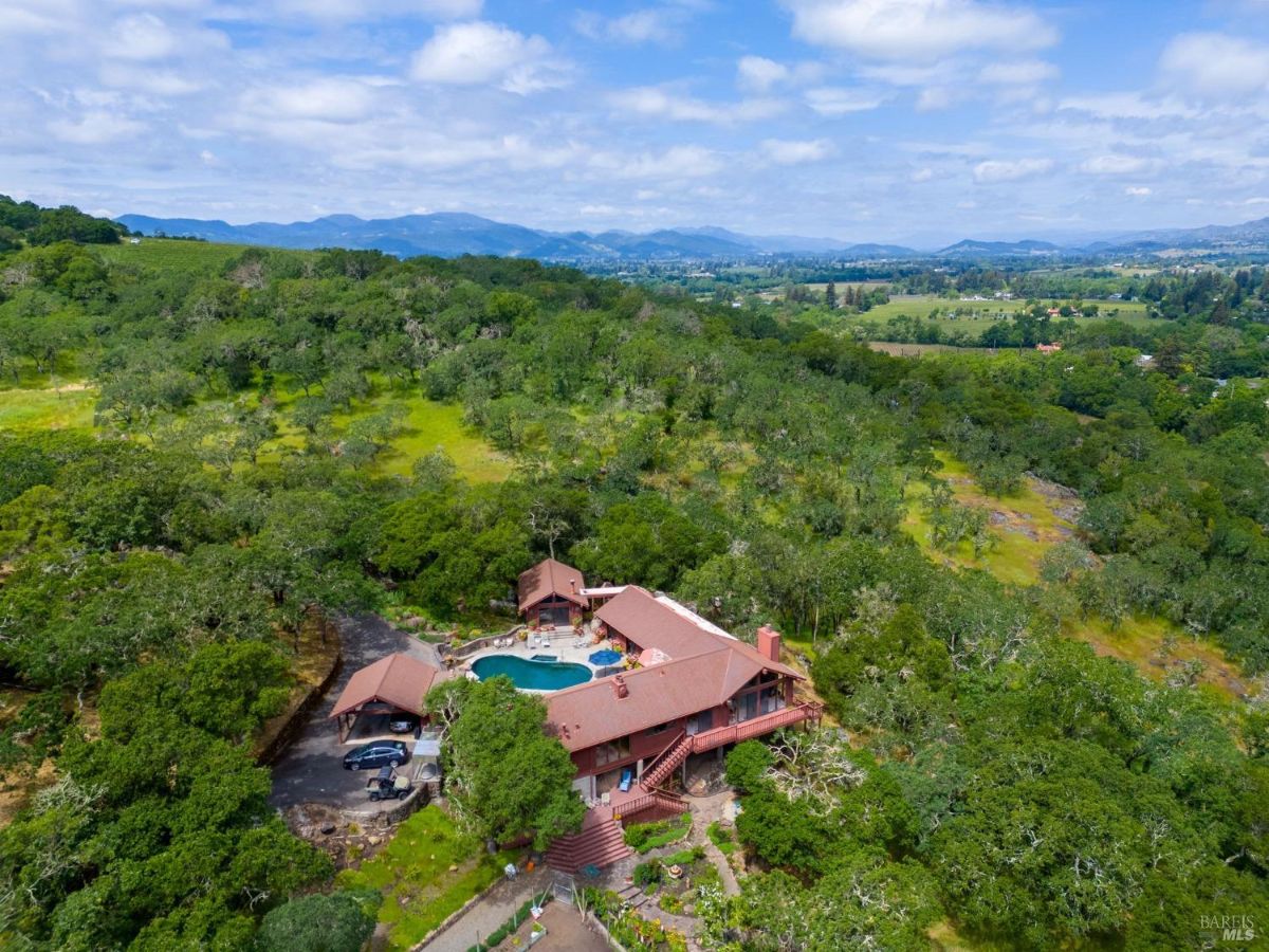 Hillside property with a large house surrounded by lush greenery and a swimming pool.