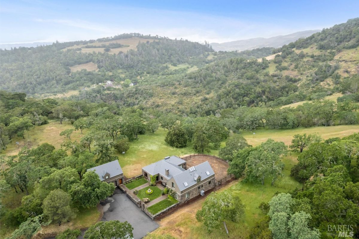 Aerial view of the property reveals a secluded estate nestled in a scenic hillside with lush greenery.