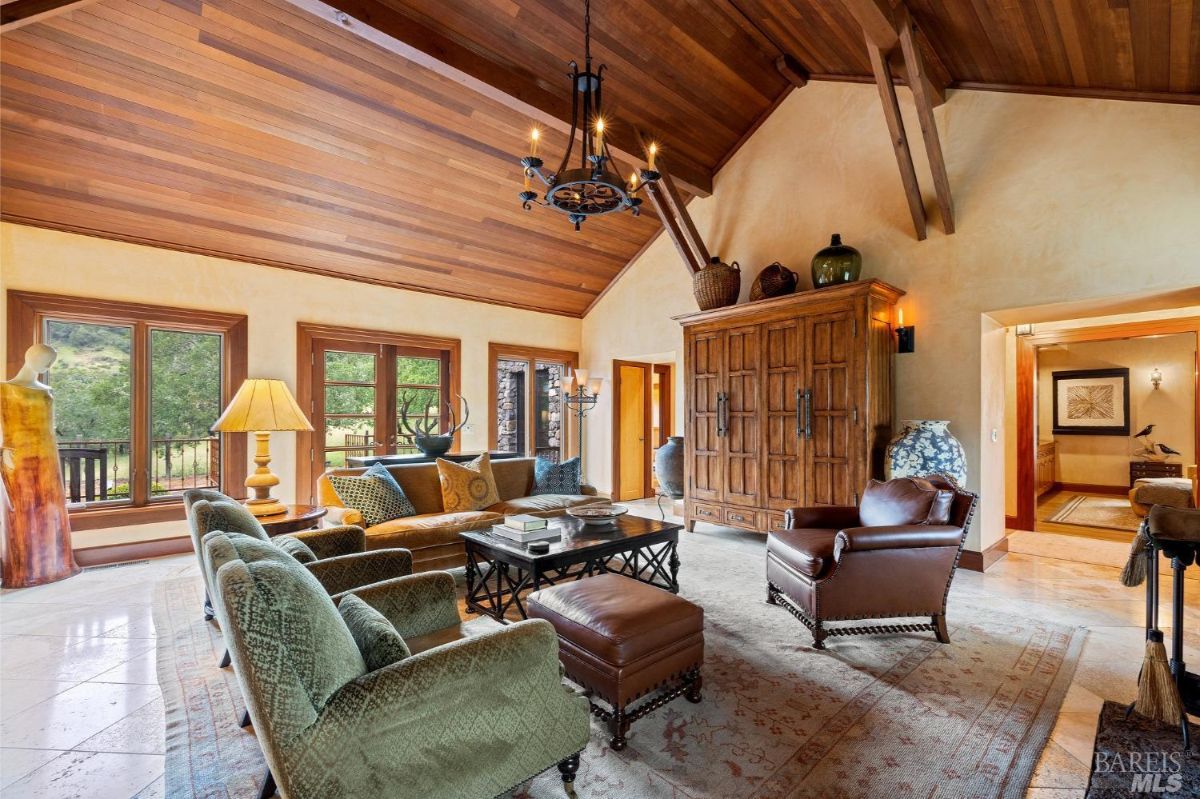 Spacious living area with large windows, textured wooden ceiling, and stylish furniture arranged around a central table.