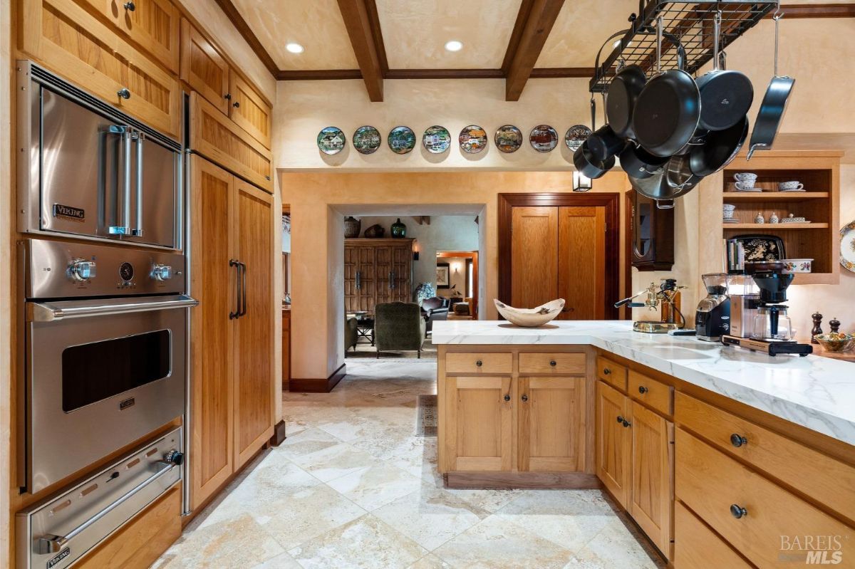 Spacious kitchen area with an island, hanging pots, wooden cabinetry, and decorative plates adorning the walls.