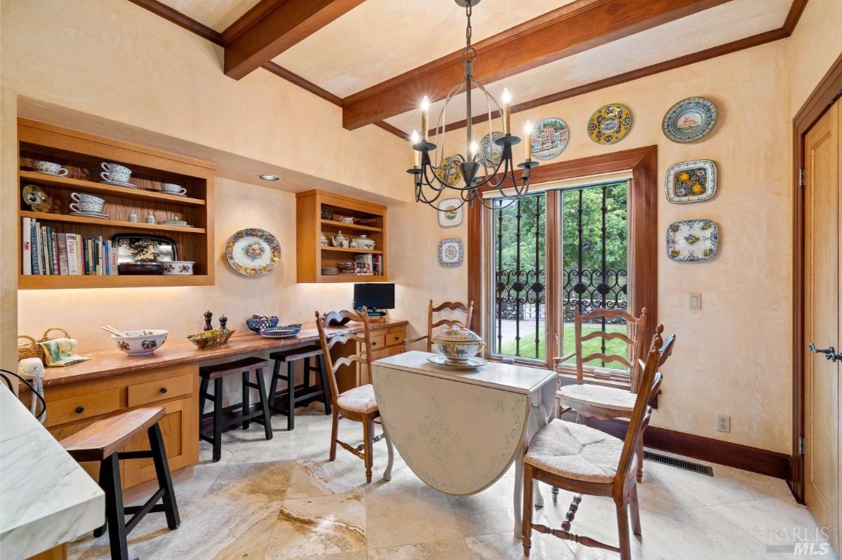 Compact breakfast nook with built-in wooden shelves, decorative plates on the walls, and a chandelier above a small table.